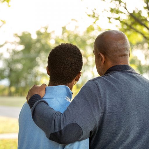 A man and boy are standing arm in arm.