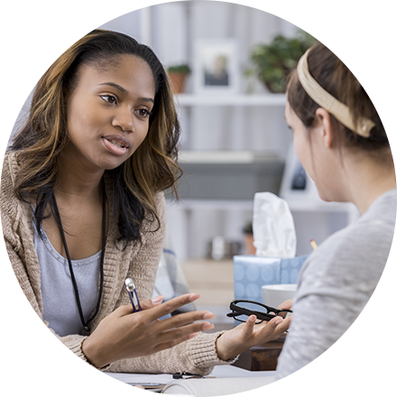 A woman sitting in front of another person holding a cell phone.