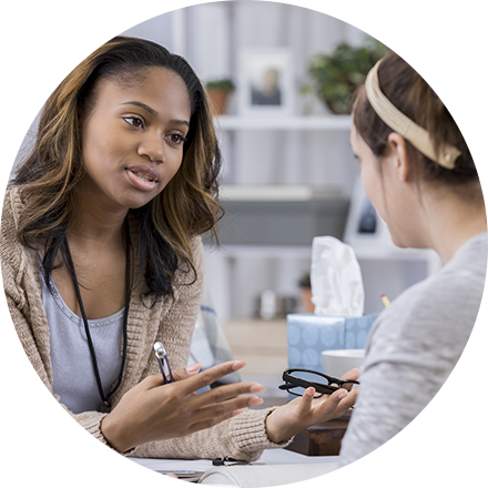 A woman sitting in front of another person holding a cell phone.